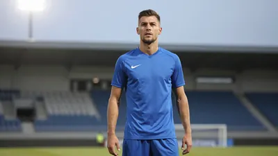A 25-year-old male footballer, wearing a solid blue kit, with a determined expression, photographed with an 85mm f/1.4...