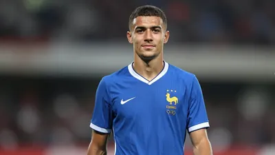 A tight waist-up crop of a young, anonymous, French defender in his early 20s, wearing a clean, blue, short-sleeved...