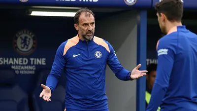 A 35-year-old Chelsea FC assistant coach, with a rugged build and receding dark hair, stands intensely in the Stamford...