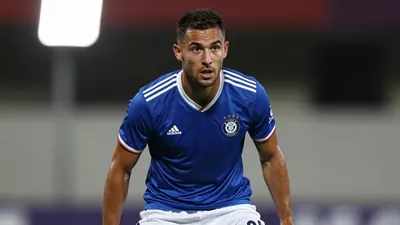 A 25-year-old male football player, with a lean build, wearing a blue jersey with white shorts, in a waist-up shot, with...