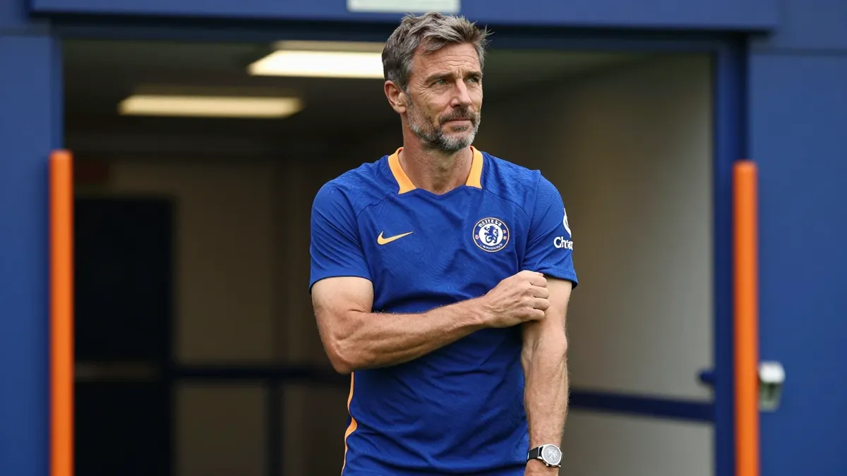A 35-year-old Chelsea FC assistant coach, with a rugged build and graying temples, stands in the Stamford Bridge tunnel...